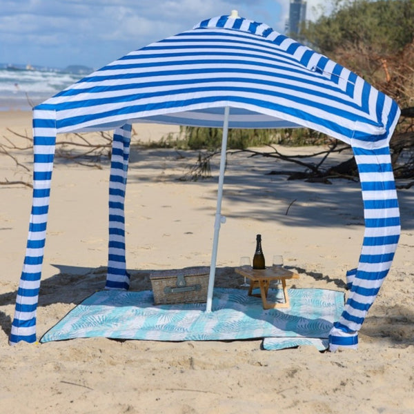 Nap and Sun light green palm leaves patterned picnic blanket set up on the beach, with a sun cabana attached.