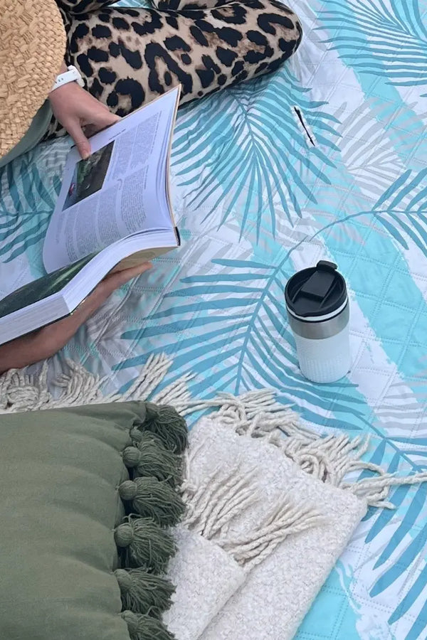 Close-up shot of a woman lying on the Leafy Vibes picnic blanket, reading a book in a relaxed outdoor setting.