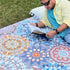 Close-up of a man lying on a mandala-patterned picnic blanket in a park, reading a book.