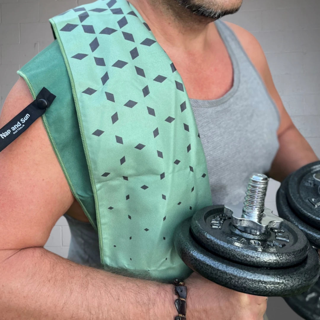 Close-up of a man exercising, holding a weight in the gym, with Nap and Sun green and black star pattern gym towel draped over one of his shoulders.