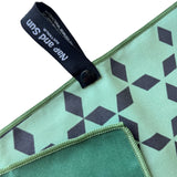 Close-up of Nap and Sun green gym towel showing the front and back. The front is a light green with a black star pattern, while the back is a darker green. A black hook with a press stud is attached for easy hanging.