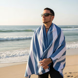 Man on a beach wearing a blue and white striped sandfree towel