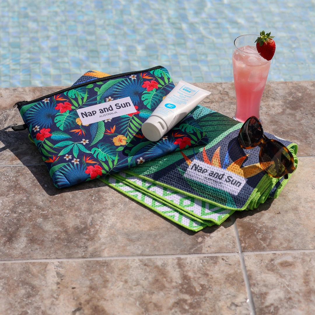 Tropical leaves pattern towel laid beside a pool with sunglasses and a cocktail.