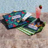 Tropical leaves pattern towel laid beside a pool with sunglasses and a cocktail.