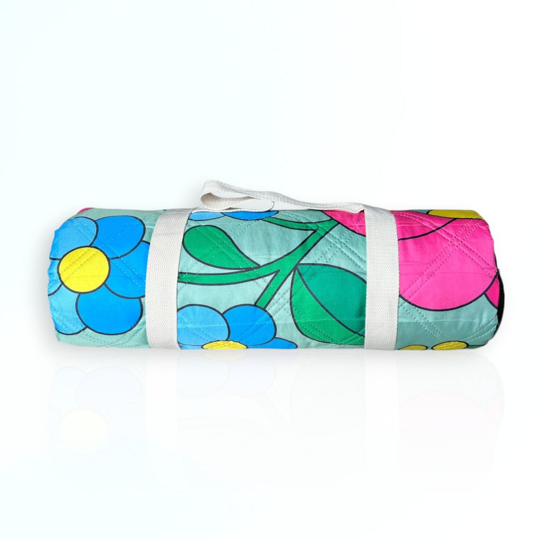 Vivid colorful flower pattern picnic blanket rolled up with a beige carry strap securely attached around it. Nap and Sun Vivid Meadow picnic blanket