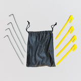 A small black bag is placed beside four yellow plastic pegs and four steel pegs, neatly arranged. Napandsun WindyCorner Picnic Pegs