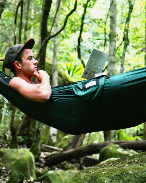 Person reading a book in a green hammock surrounded by trees 