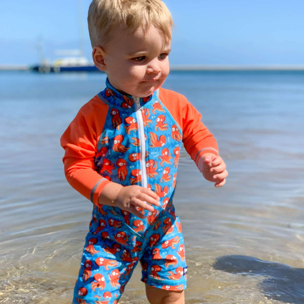 Child wearing a blue and red swimsuit with octopus pattern at the beach