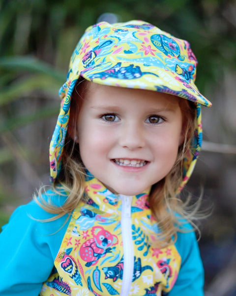 Child wearing a colorful raincoat and hat with a floral pattern, standing outdoors.