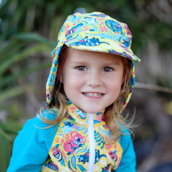 Child wearing a colorful raincoat and hat with a floral pattern, standing outdoors.
