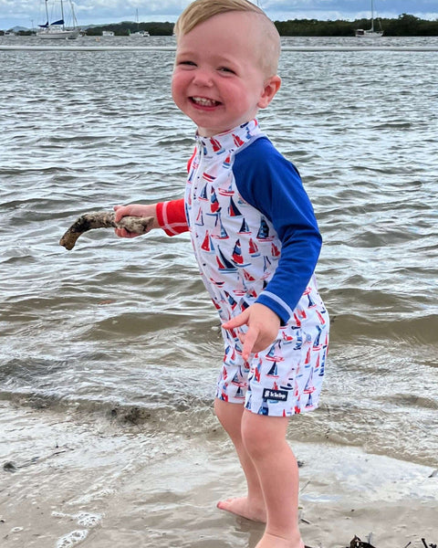 Child in a one piece swimsuit standing on a beach holding a stick