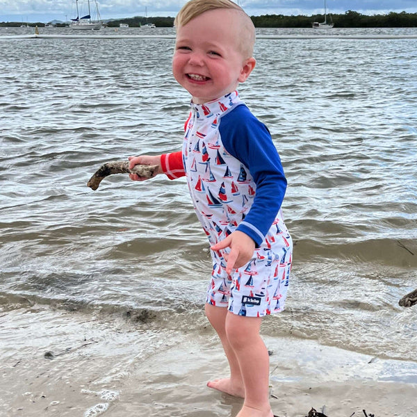Child in a one piece swimsuit standing on a beach holding a stick
