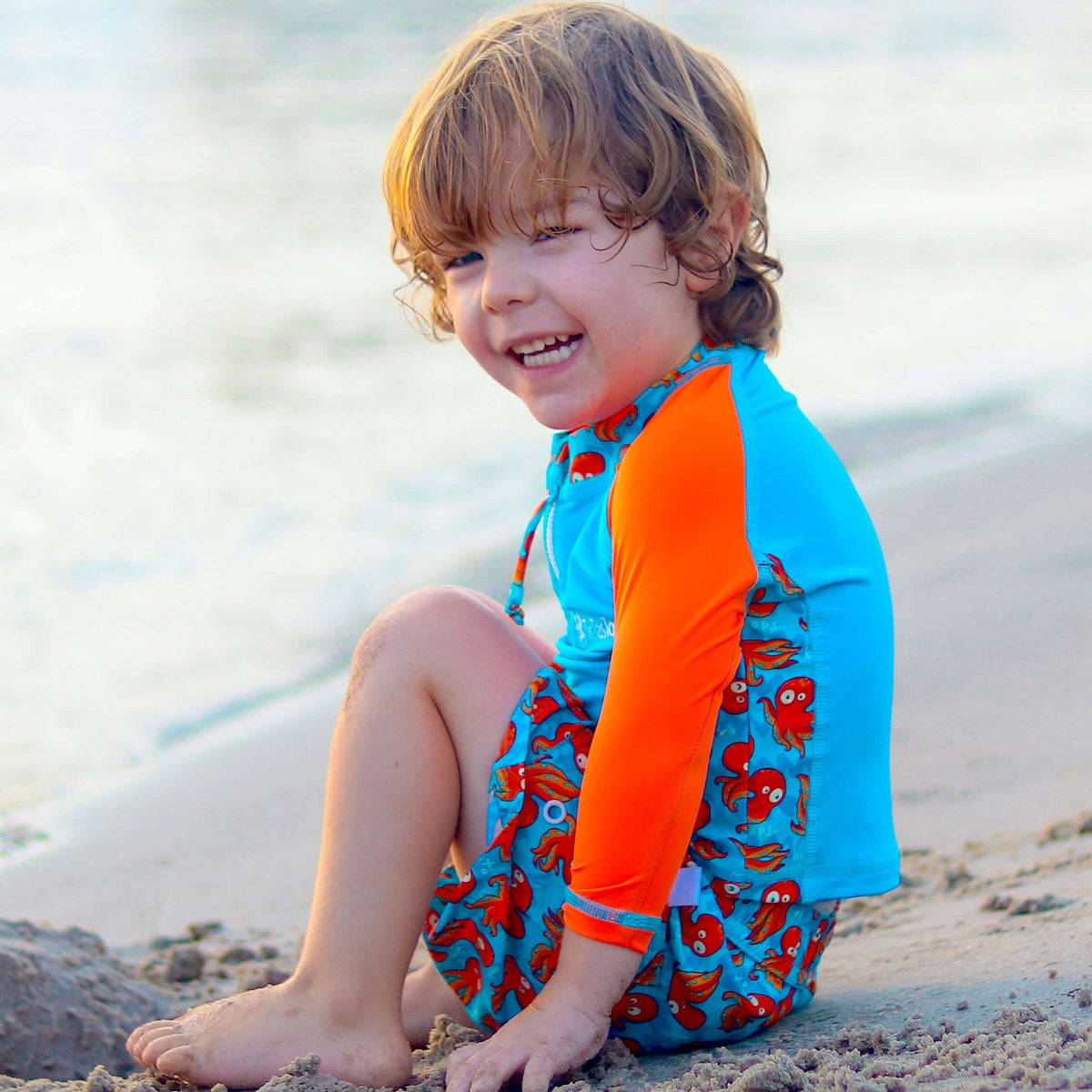 Child wearing a blue and orange swimsuit with crab pattern on a beach