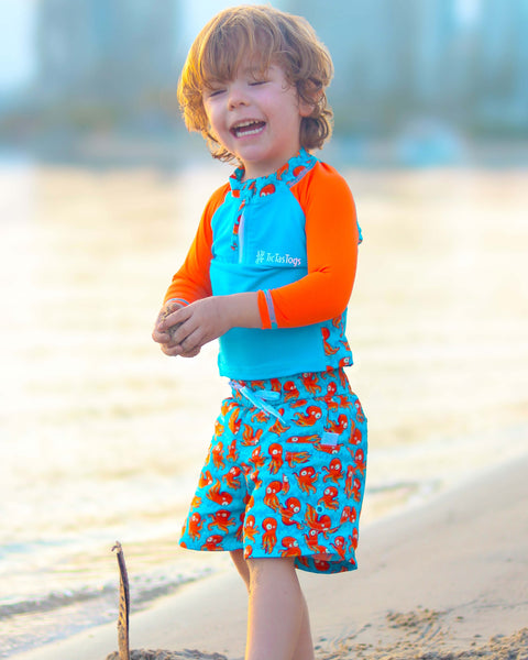 Child wearing a colorful outfit with a blue and orange top and red octopus skirt on a beach.