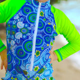 Child wearing a blue and green patterned rash guard with a blurred background