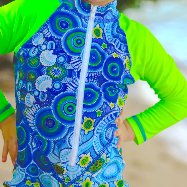 Child wearing a blue and green patterned rash guard with a blurred background