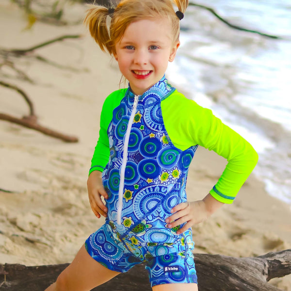 Child wearing a blue and green patterned swimsuit on a beach