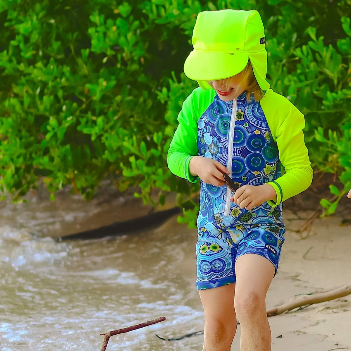 Child in a blue and green swimsuit with a bright yellow hat on a beach.