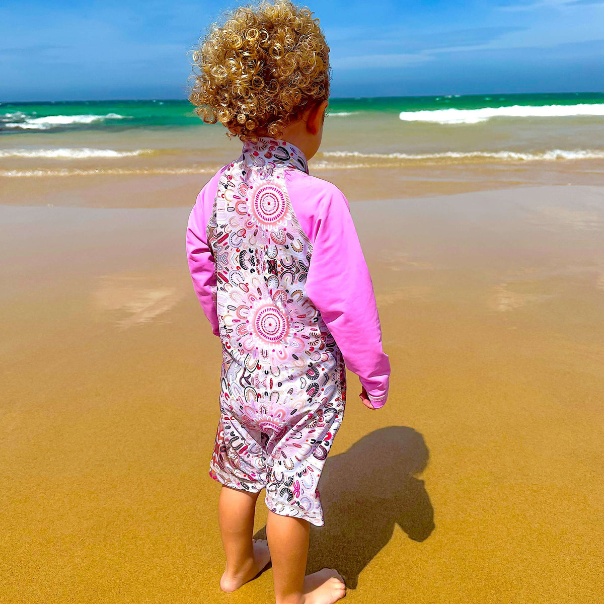 Child wearing a pink and patterned swimsuit on a beach
