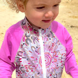 Child wearing a pink and patterned swimsuit on a beach