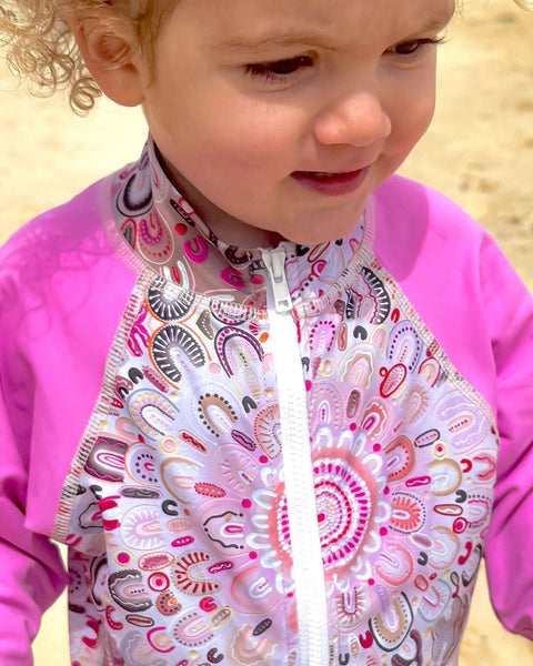 Child wearing a pink and patterned swimsuit on a beach