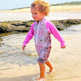 Child in a pink and white patterned swimsuit walking on a beach.