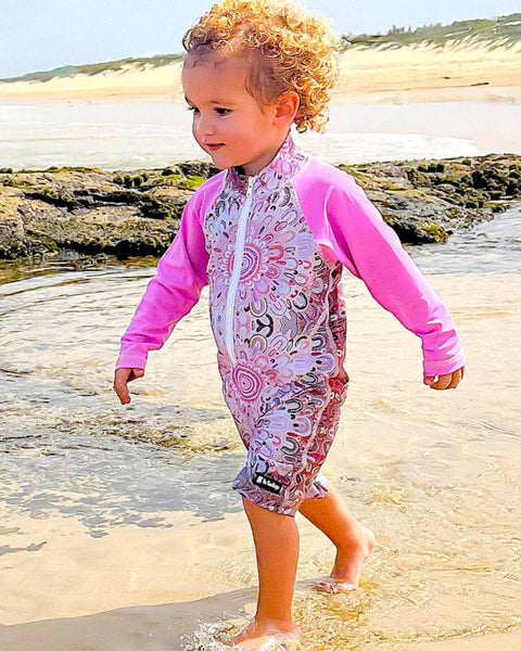 Child in a pink and white patterned swimsuit walking on a beach.