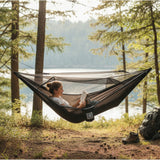 Person reading a book in a hammock by a lake surrounded by trees
