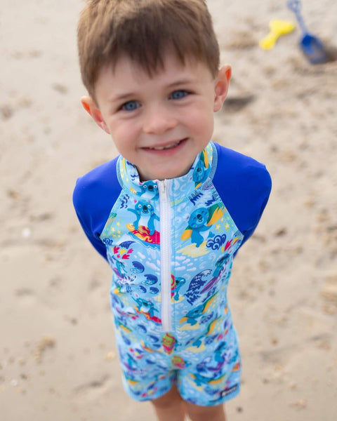Child wearing a blue swimsuit with koala designs on a sandy beach
