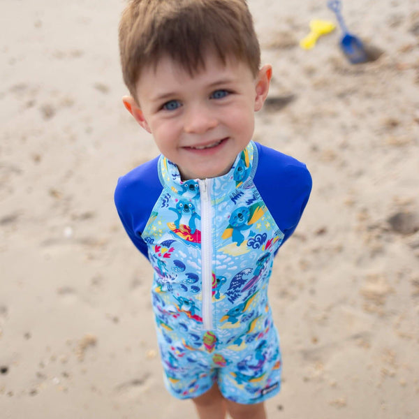 Child wearing a blue swimsuit with koala designs on a sandy beach