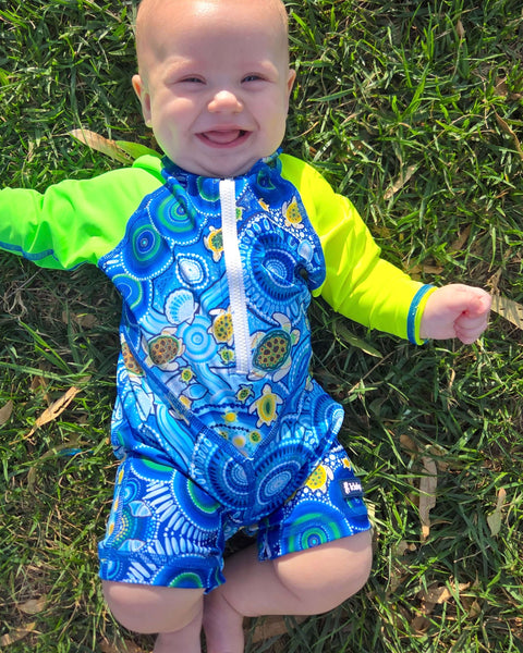 Baby wearing a blue and green swimsuit with turtle pattern on grass