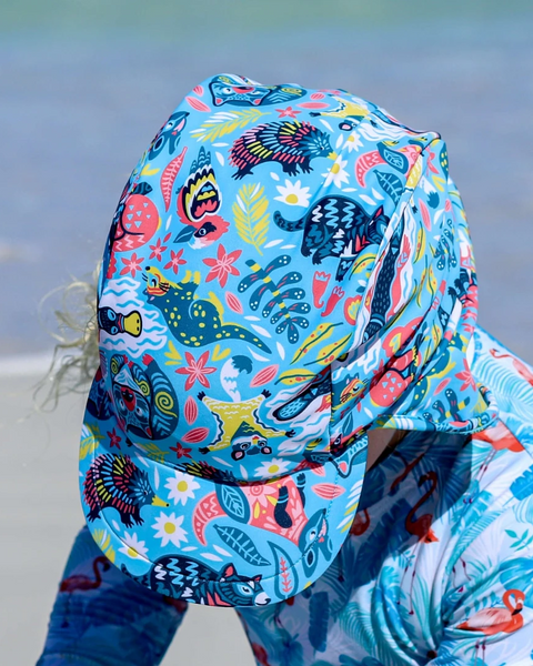 Child wearing a colorful shark-themed swimsuit with a hood on a beach.