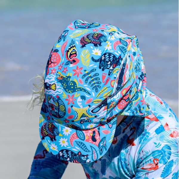 Child wearing a colorful shark-themed swimsuit with a hood on a beach.
