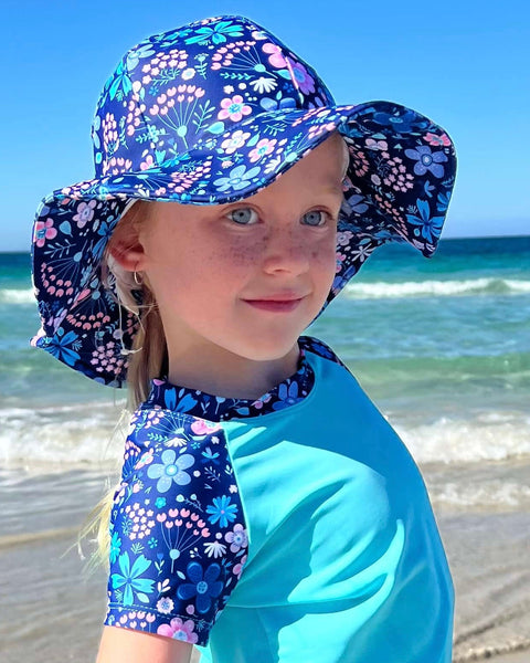 Child wearing a floral sun hat and matching scarf on a beach