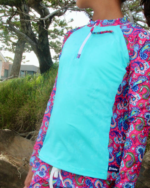 Person wearing a colorful long-sleeve shirt with a paisley pattern on a beach.