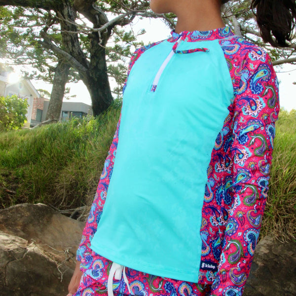 Person wearing a colorful long-sleeve shirt with a paisley pattern on a beach.