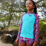 Young girl wearing a colorful rash guard and shorts outdoors near rocks and trees