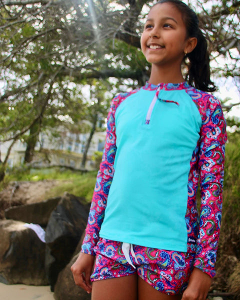 Young girl wearing a colorful rash guard and shorts outdoors near rocks and trees
