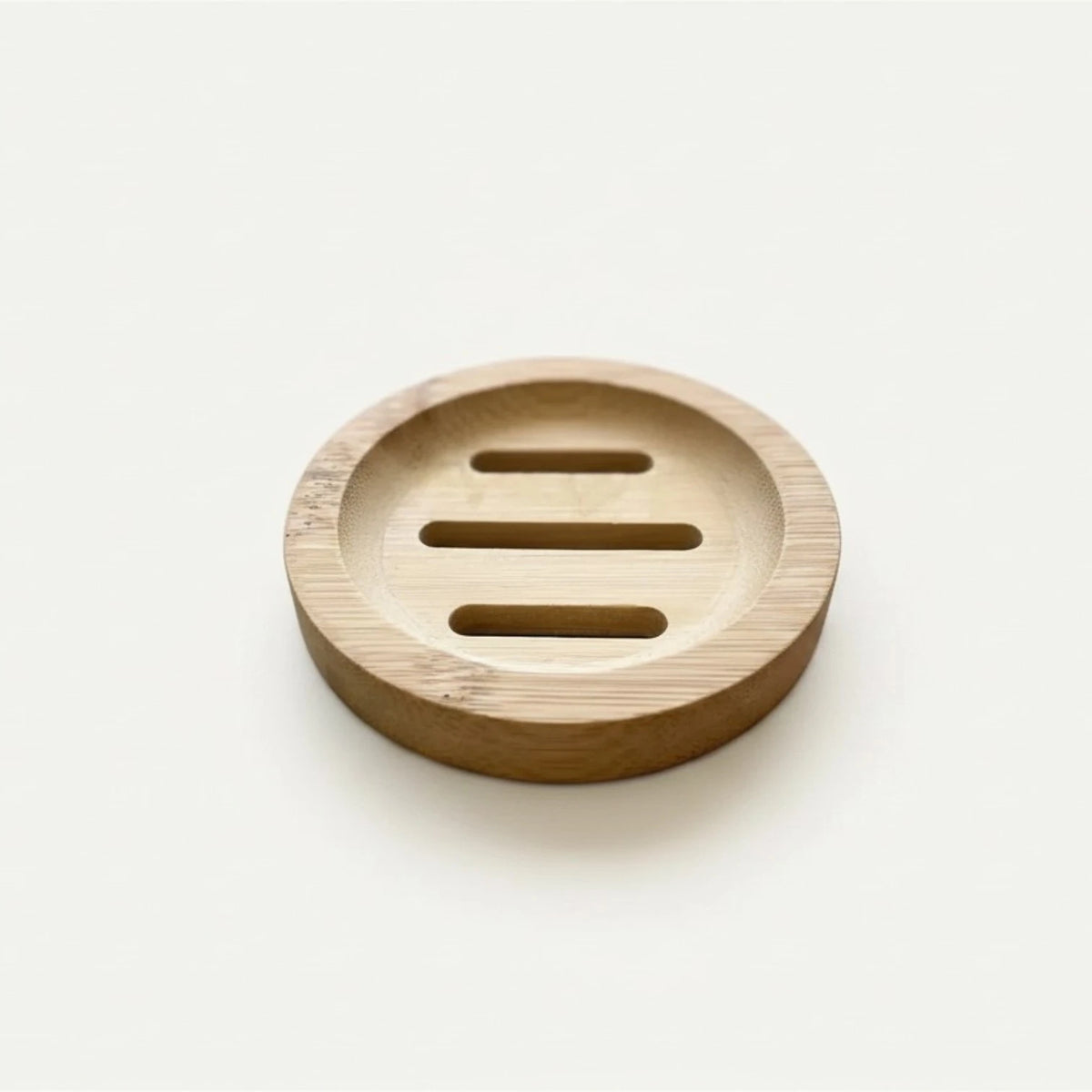 A round natural bamboo soap dish with three horizontal slots, photographed on a clean, solid off-white background.