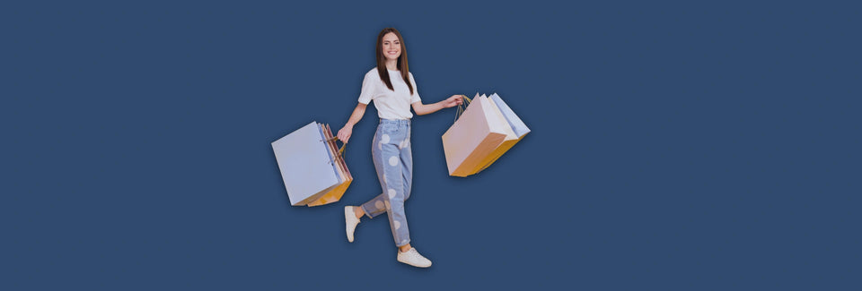  Woman standing against a dark blue background, holding multiple paper shopping bags.