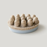 An oval shaped massage soap bar with a light blue base and beige, photographed on a neutral light gray background.