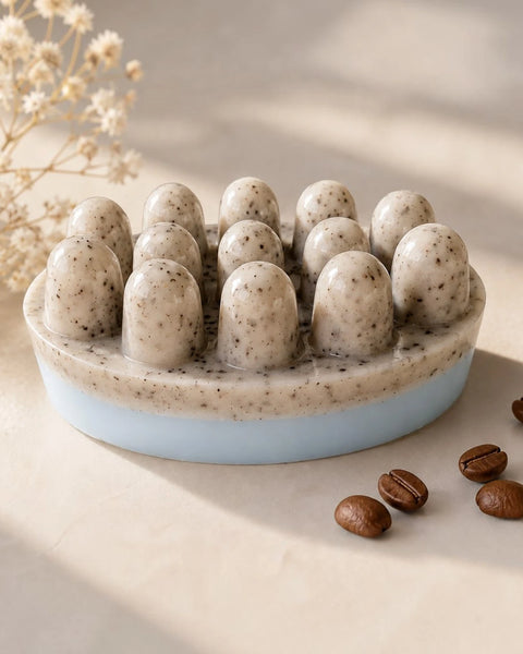 Handmade coffee soap bar with real coffee grounds, a natural speckled top and soft light blue base, styled on a beige surface with coffee beans and dried flowers.