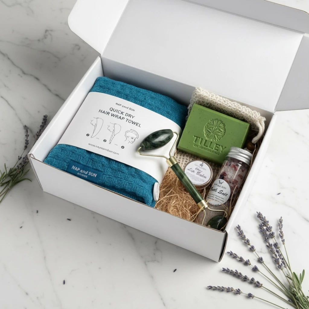 Gift set with teal hair wrap towel, soap, face roller, bath salt, lip balm on a counter.
