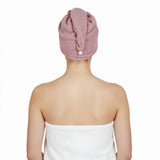 A person shown from the back wearing a dusty pink textured microfiber hair wrap on their head and a white towel around their shoulders, against a plain white background.