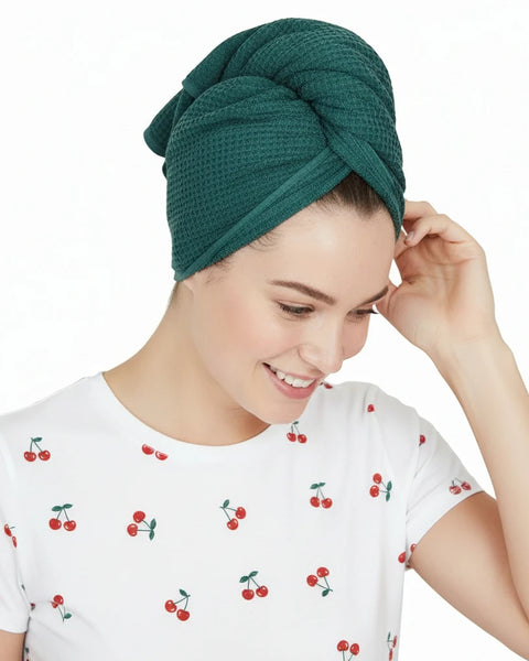 Woman wearing a teal hair towel on her head with a white shirt.