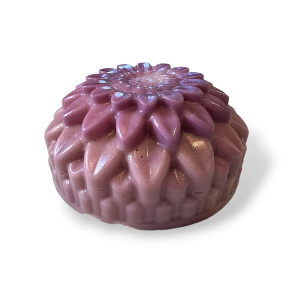 A single round, textured soap with a floral top pattern, shown on a plain white background. The soap has a glossy finish and features a color gradient transitioning from a dusty mauve-pink at the base to a deeper purple at the top.