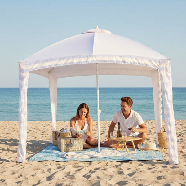 two people sitting under a cabana on a light green picnic blanket on a beach.