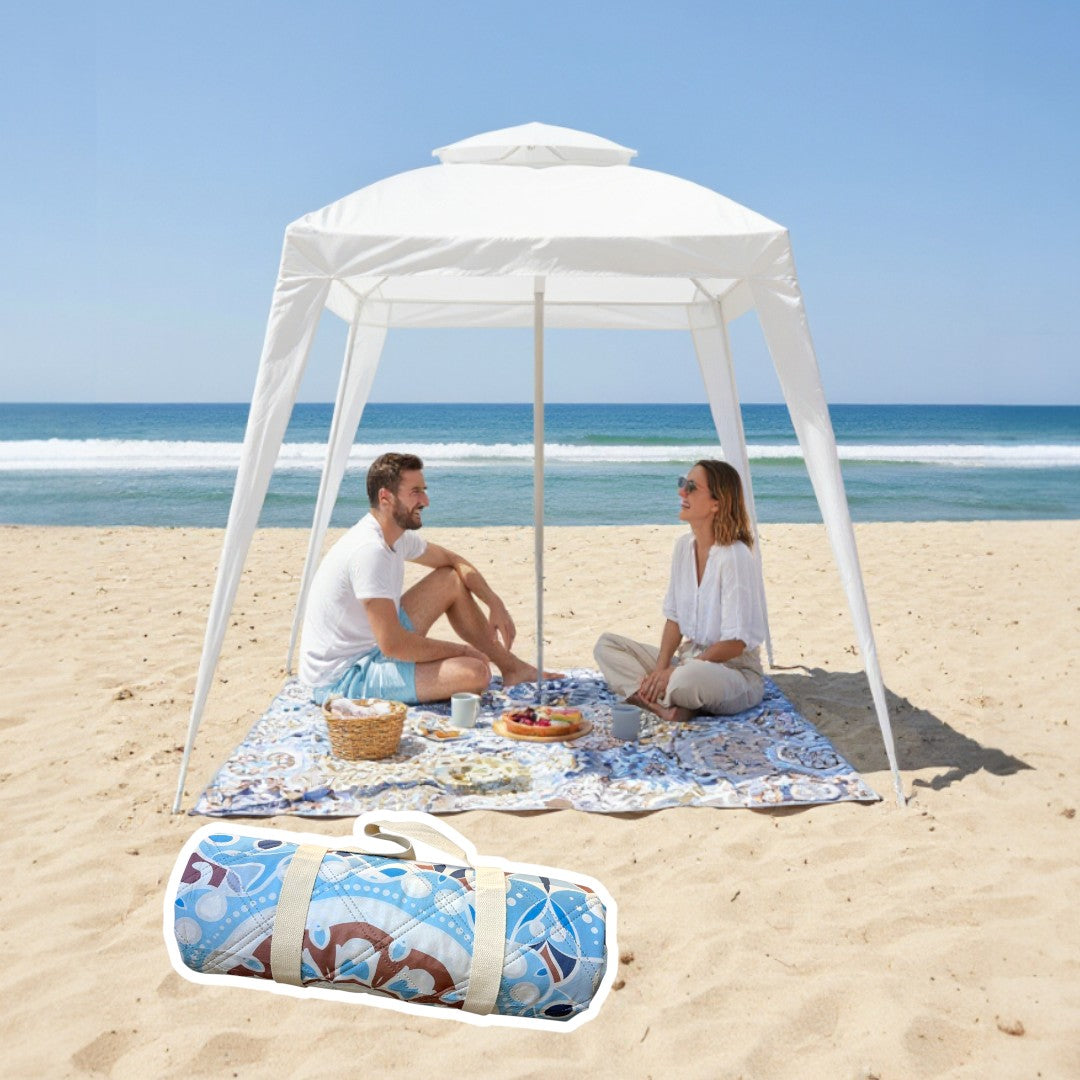 Two people sitting under a cabana on a mandala patterned picnic blanket at the beach.