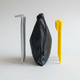Black pouch with yellow sand pegs and metal pegs on a light gray background.