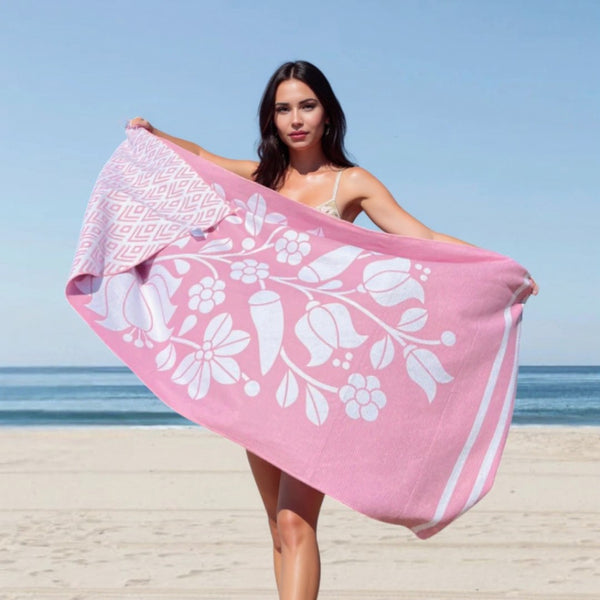 Woman holding a pink beach towel with white floral patterns on a beach.